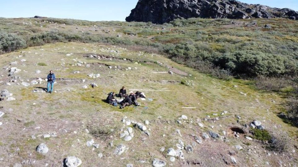 Archaeological excavation site in Greenland with researchers surveying ruins in a remote tundra landscape.