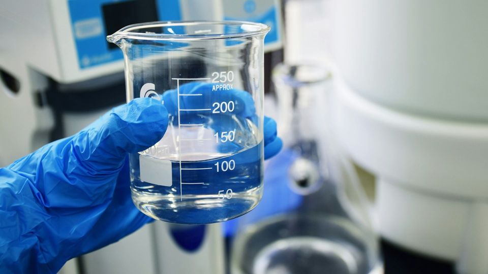 Laboratory beaker containing clear liquid held by a gloved hand.