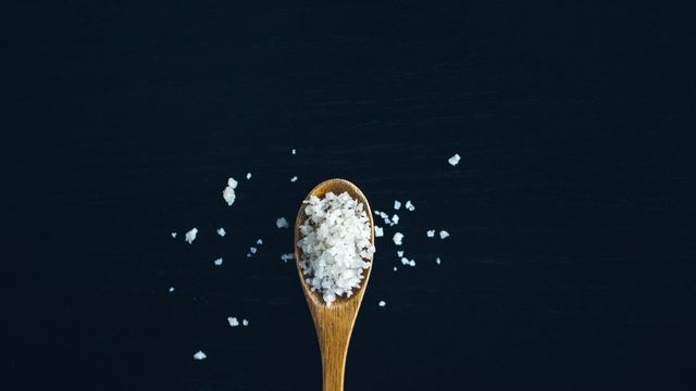 Wooden spoon filled with coarse salt crystals on a dark background. 