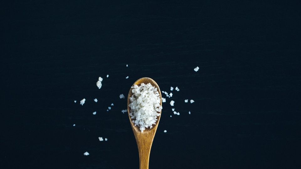 Wooden spoon filled with coarse salt crystals on a dark background.