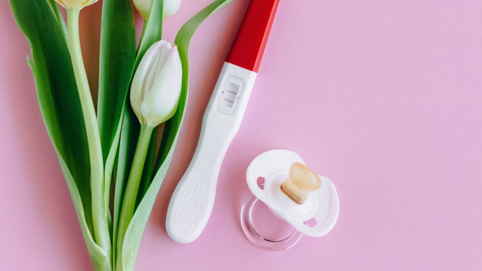 Tulips, a pregnancy test, and a pacifier laid on a pink background.