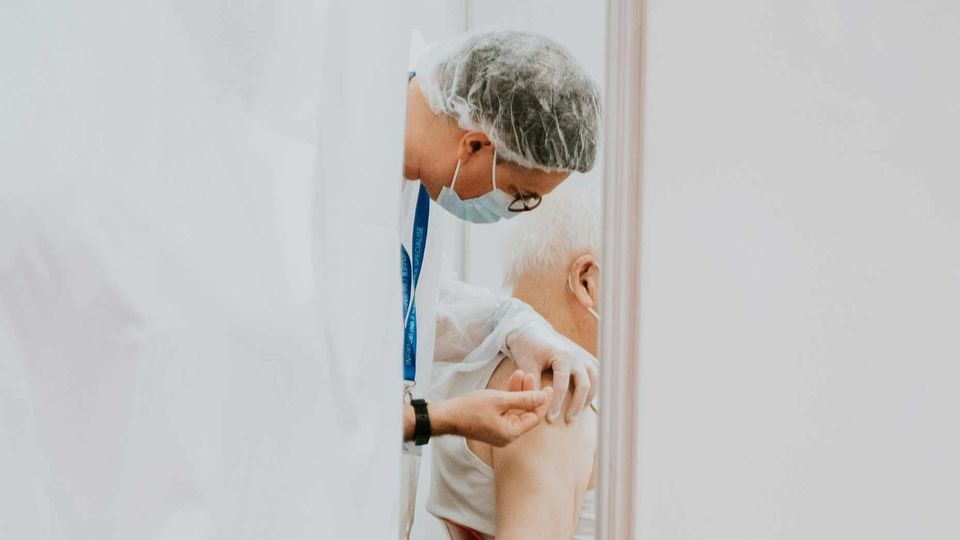 A healthcare worker, wearing a face mask, administering a vaccine into an elderly person's upper arm.