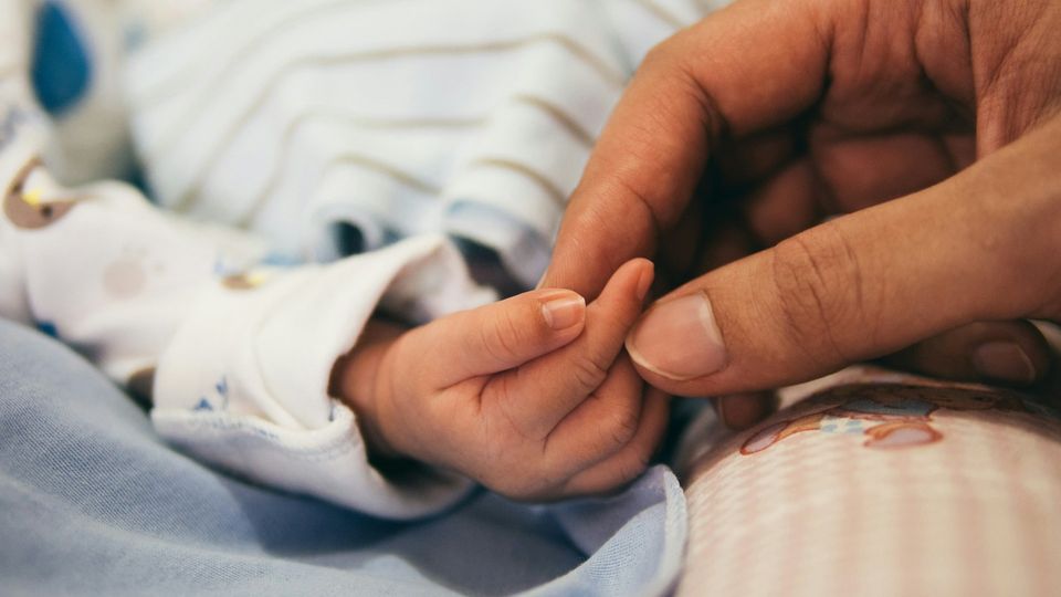 Close-up of an adult hand holding the hand of a newborn baby.