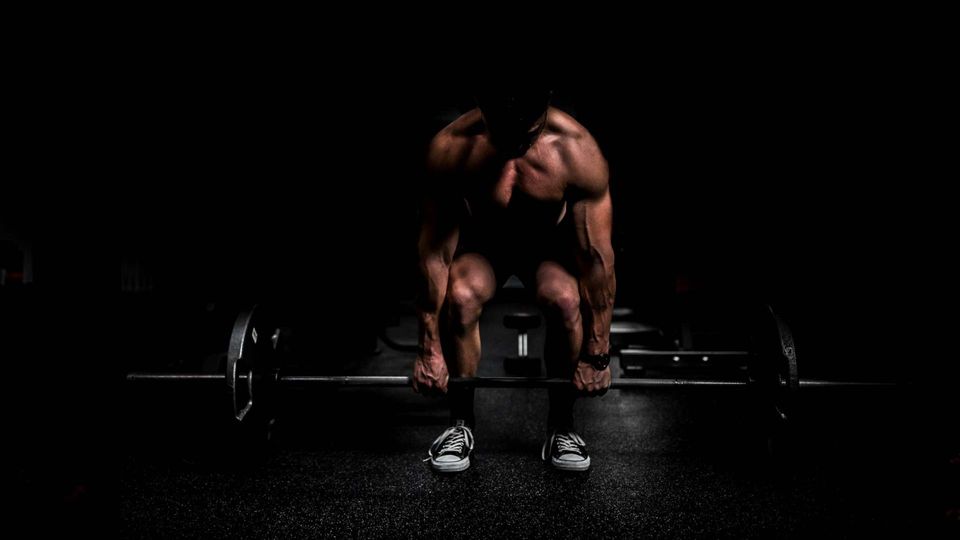 Muscular athlete performing a heavy deadlift in a dark gym to build muscle strength.