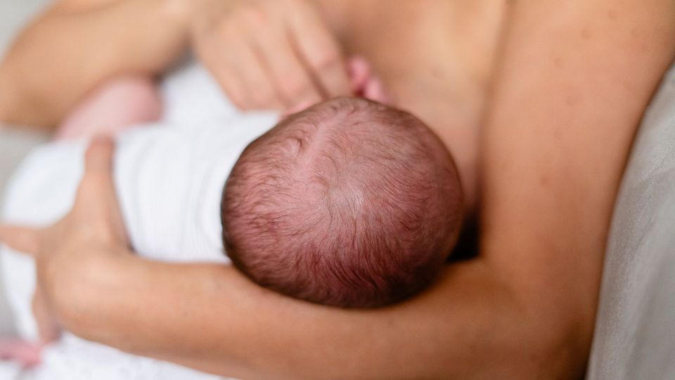 Mother breastfeeding a newborn baby while holding the infant close in her arms.