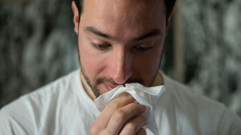 Man holding a tissue to his nose.