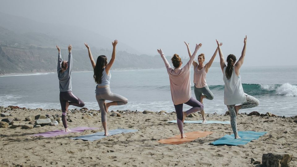 Women practicing yoga in tree pose on a beach.