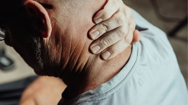Close-up of hand pressing back of neck, highlighting neck pain and muscle tension. 