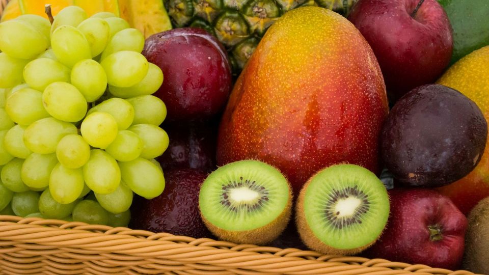 Basket of fresh fruit with grapes, mango, kiwi, apples, and pineapple.