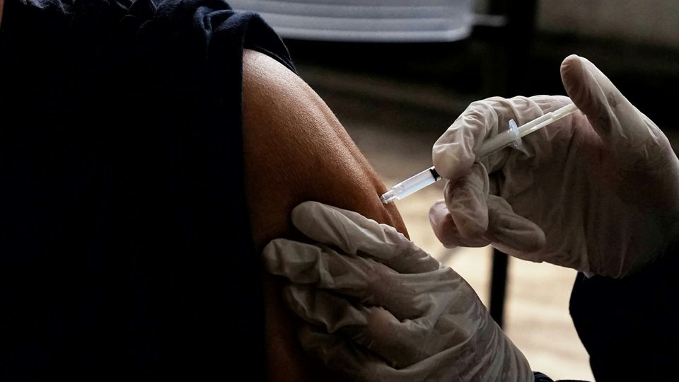 Healthcare professional administering a vaccine injection in the upper arm while wearing gloves.