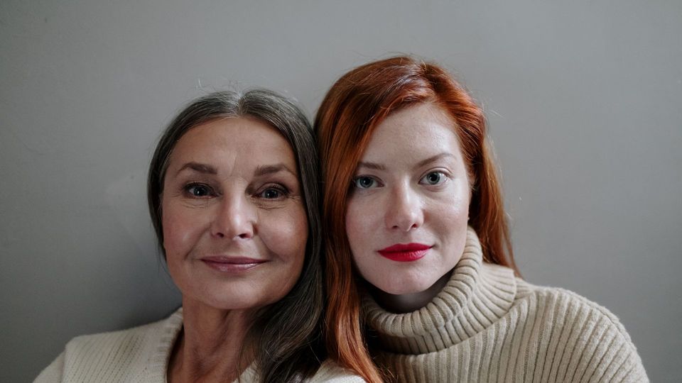 An older woman and a younger woman sit side-by-side, their faces close together.