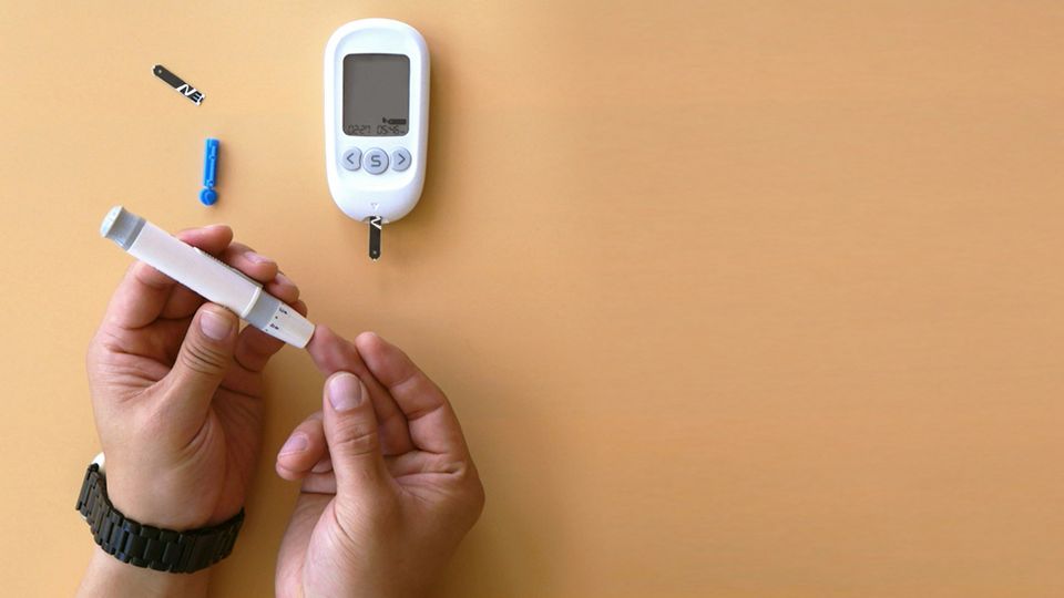 Birds-eye view of a person carrying out a finger-prick glucose test, with the monitor and test strip beside them.