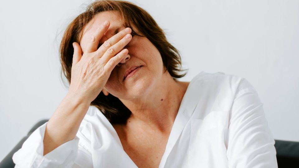 Woman with short dark hair, covering her face with one hand, appearing in discomfort.