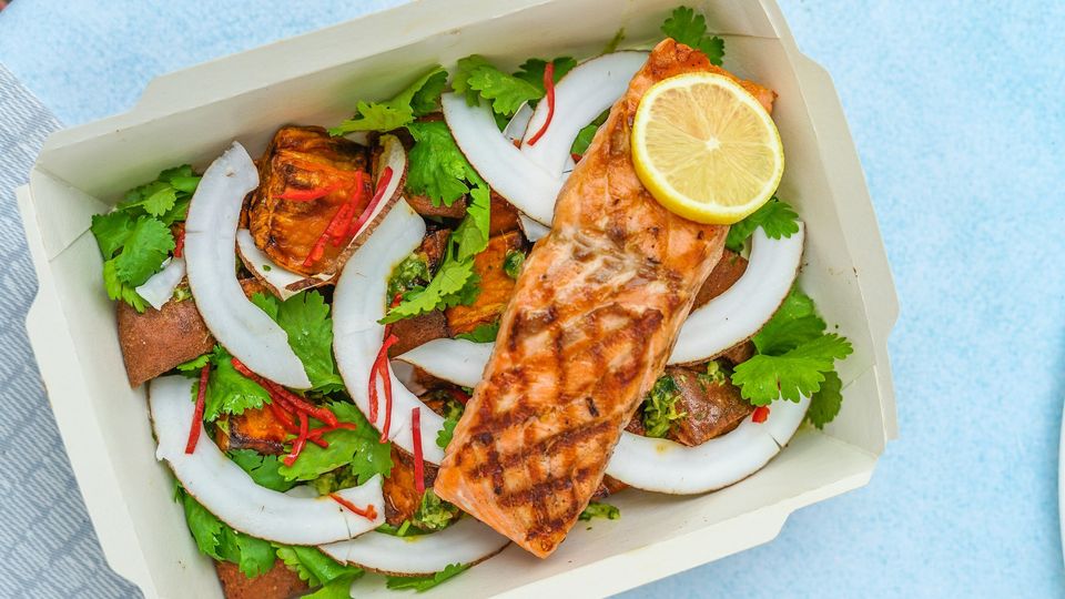 A cardboard food box containing salad and a fillet of grilled salmon.