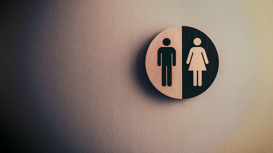 Unisex restroom sign displaying male and female symbols on a wall.