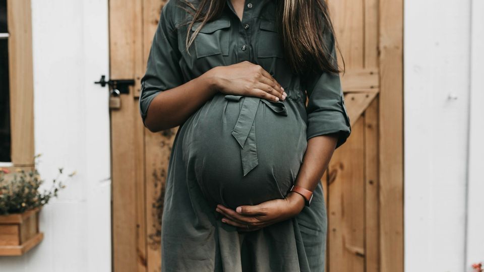 Pregnant woman holding her baby bump while standing outdoors.