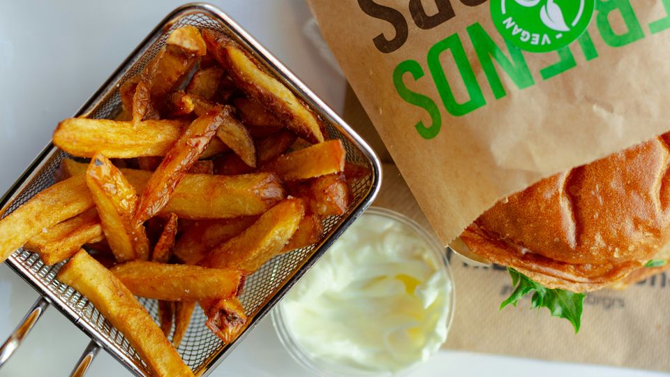 A takeaway vegan burger and chips, wrapped in packaging that reads "vegan friendly".