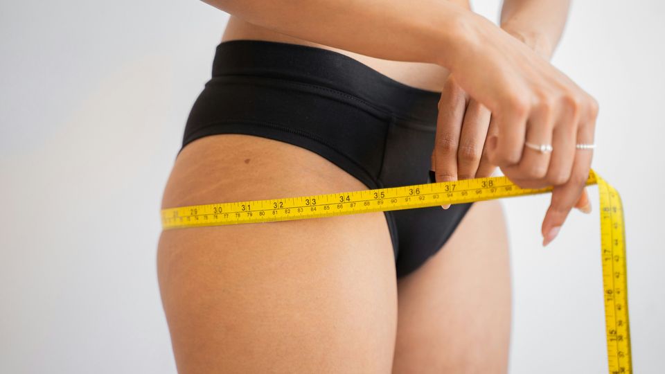 Woman holding a yellow measuring tape around her hips while wearing briefs.