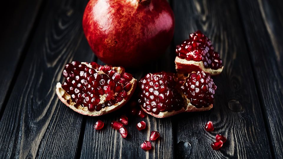 Fresh organic pomegranate with opened sections revealing juicy seeds on a wooden table.