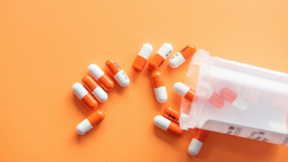 Orange and white prescription pills spilled from a medication bottle on an orange background.