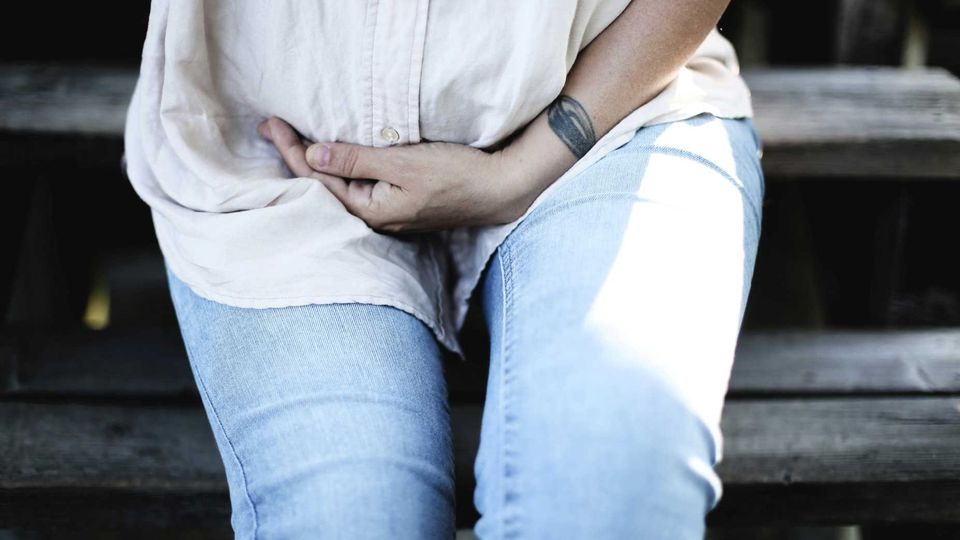 Person sitting on outdoor steps holding their lower abdomen, illustrating abdominal pain symptoms.