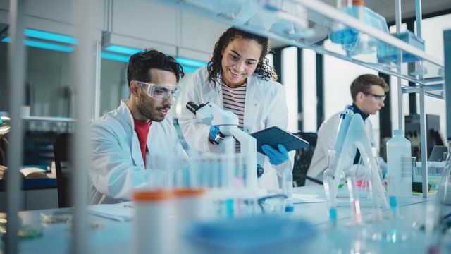 Researchers in a lab, surrounded by glassware and cool-toned blue light. 