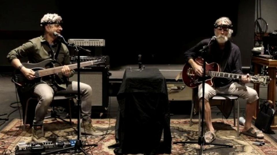 Musicians performing a live acoustic rehearsal with guitars, microphones, and audio equipment.