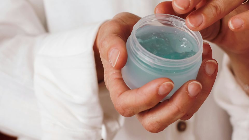 Close-up of hands holding an open jar of clear gel.