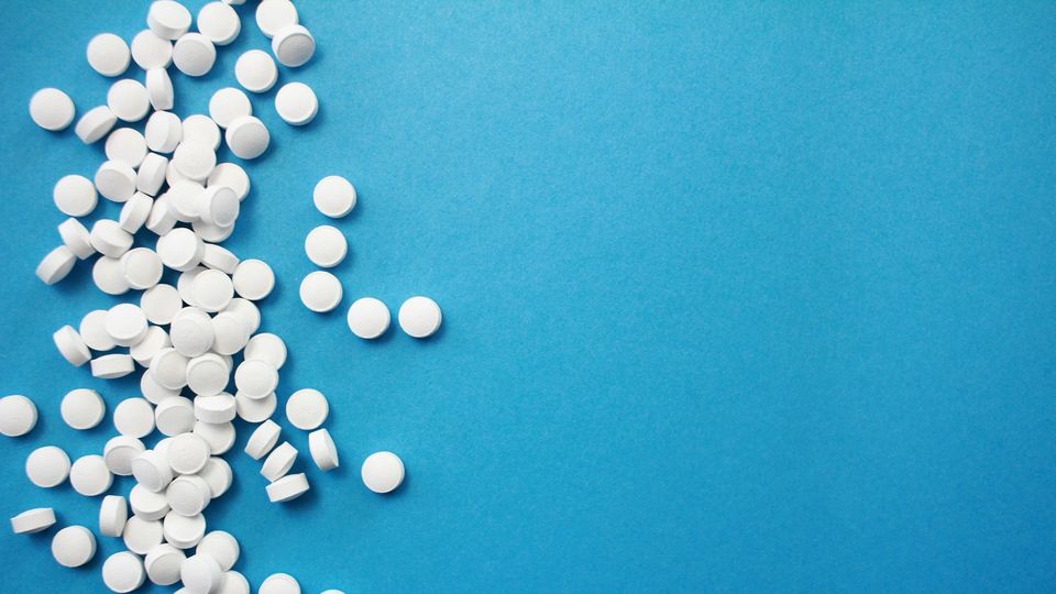 White pills scattered to the left of the frame on a blue background.