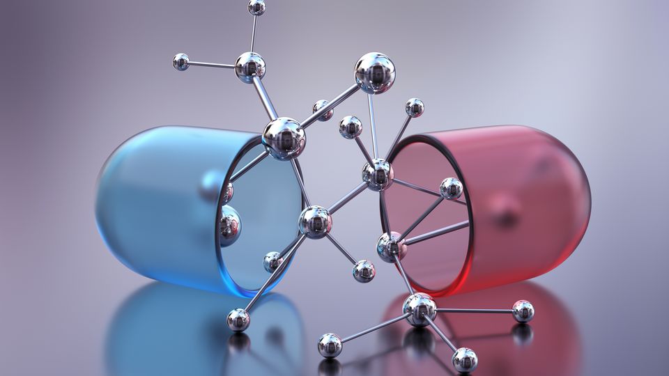 Red and blue medicinal capsule split in half. Between the two halves is a silver ball and stick model.