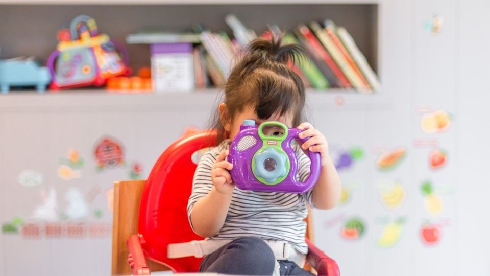 A toddler holds a plastic camera to their face.