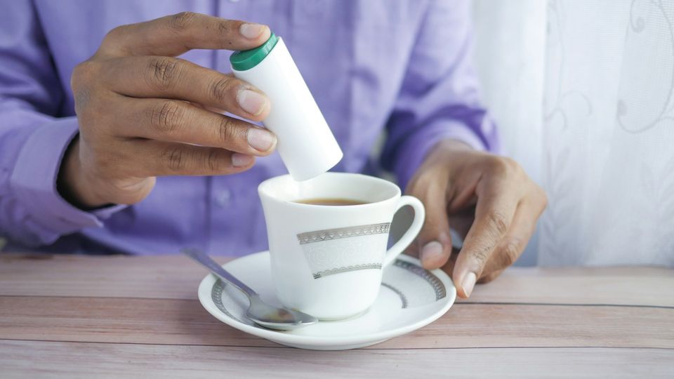 Hand adding a sweetener to a cup of coffee.