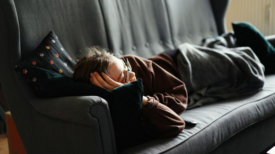 Woman resting on a couch under a blanket.