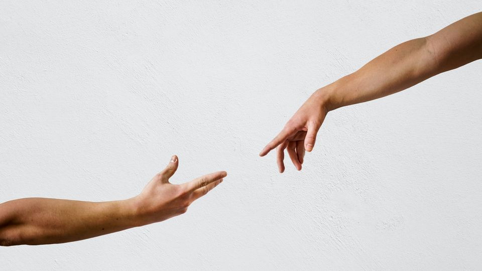 Two hands reaching toward each other against a plain background, fingertips nearly touching.