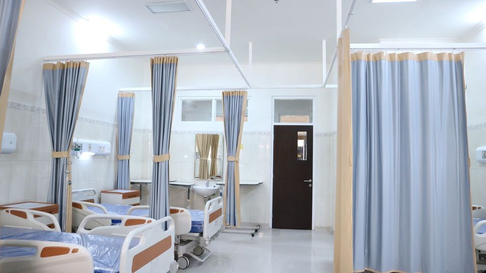 Clean hospital ward with patient beds and privacy curtains in a modern healthcare facility.