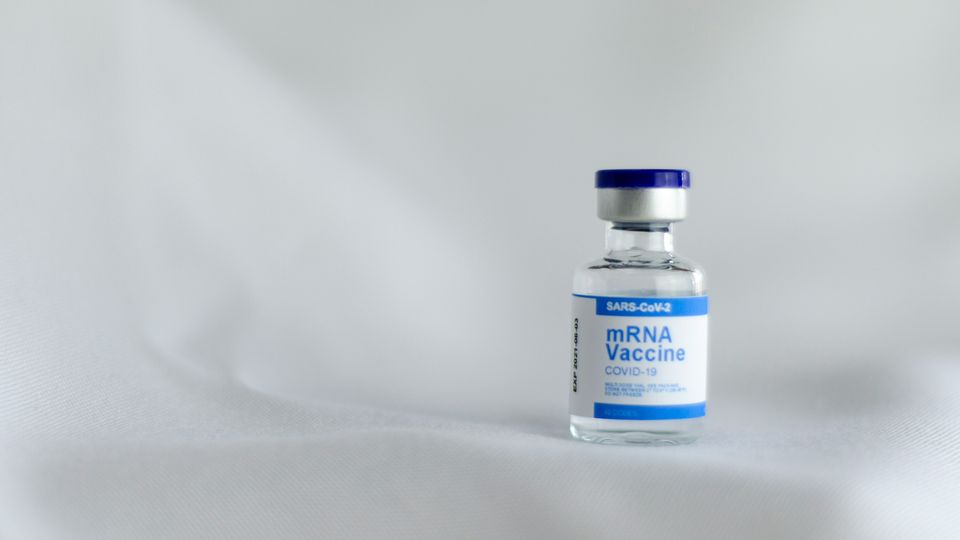 Single mRNA vaccine vial placed to the right of the frame, against a plain white backdrop.
