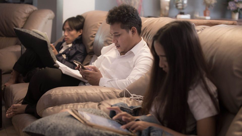 Three people sitting on a sofa, engaging in sedentary behavior.