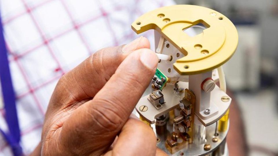 Researcher inserting a sample into a scientific probe during laboratory instrument preparation.