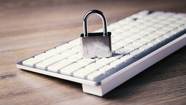 A silver padlock, sitting on top of a white computer keyboard. 