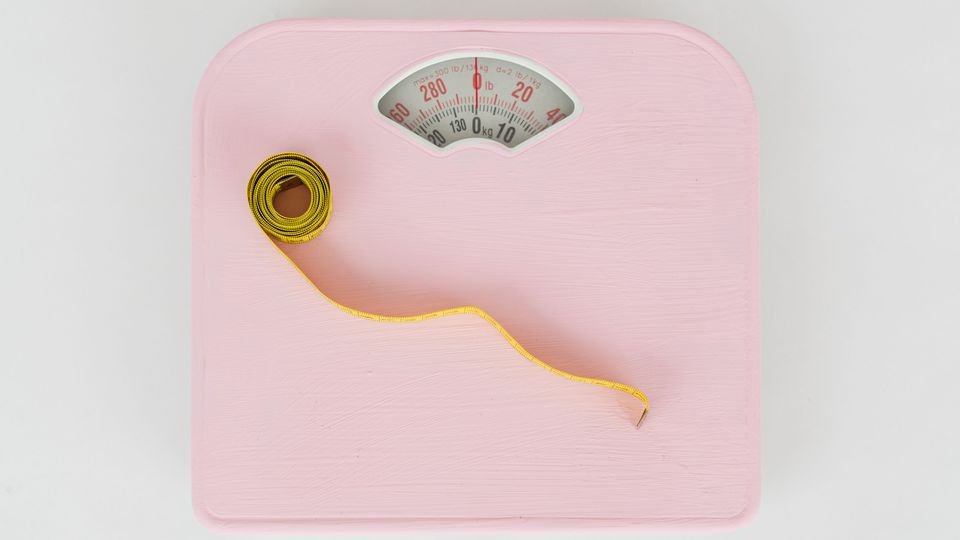 Birds-eye view of a pink weighing scale with a yellow measuring tape placed on top of it.