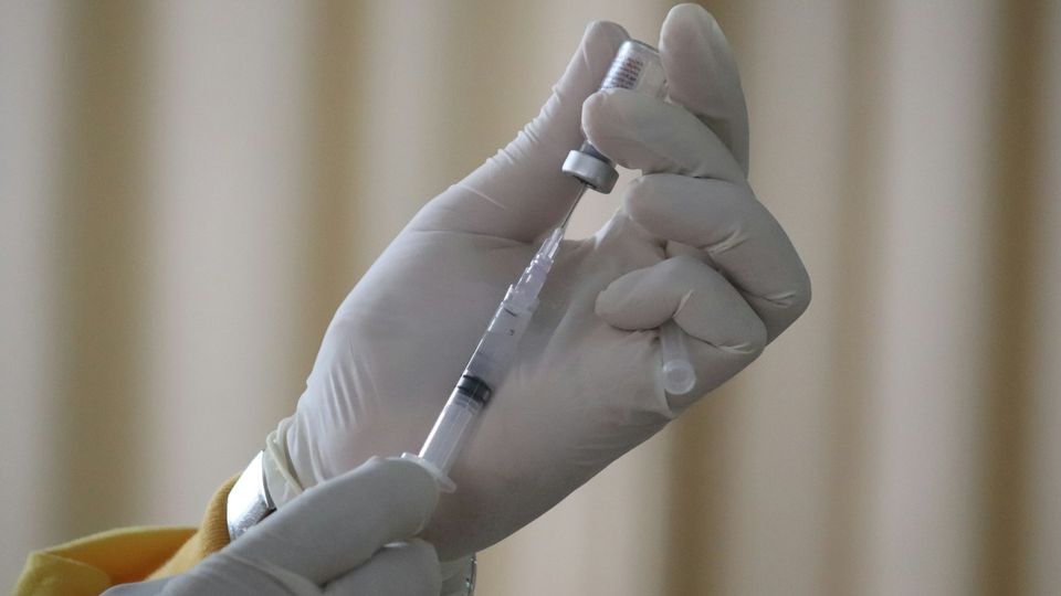 Healthcare worker preparing a syringe by drawing medication from a vial before an injection.