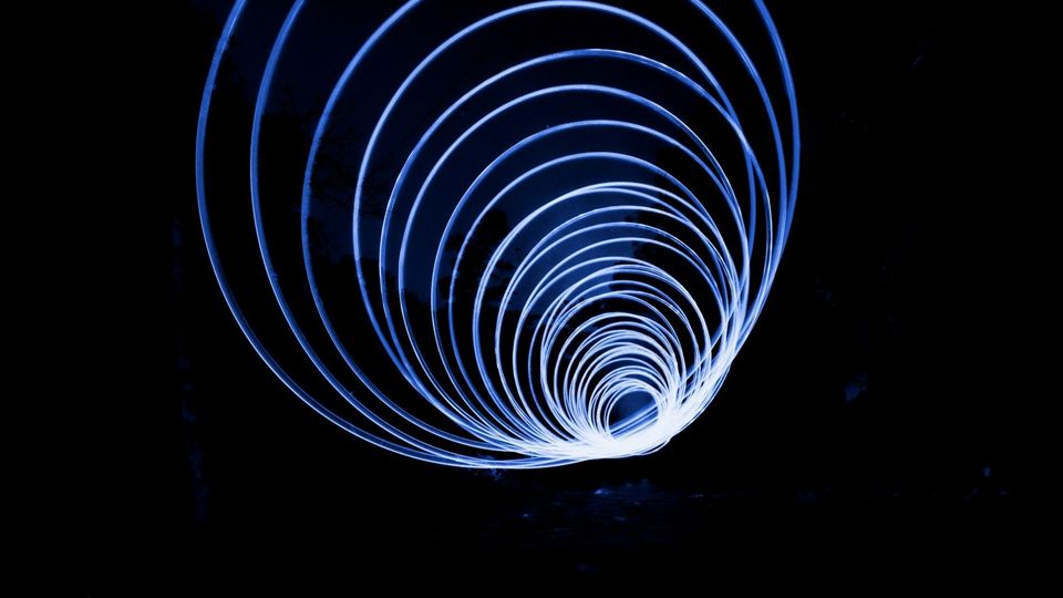 Abstract blue light spiral creating concentric circular trails against a dark background.