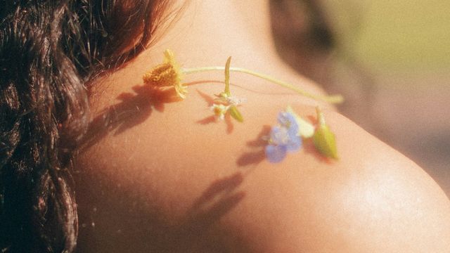 Close-up of a woman's bare shoulder with an assortment of small flowers arranged on top of it. 