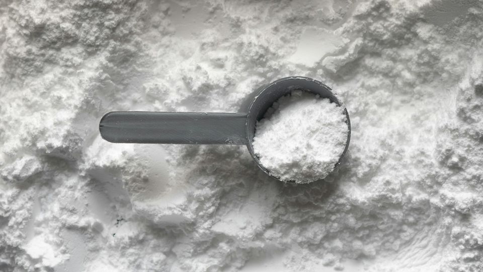 Plastic scoop filled with white creatine powder resting on a pile of loose supplement powder.