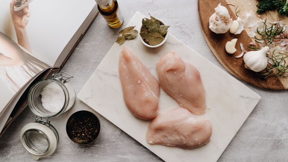 Raw chicken breasts with garlic, herbs, salt, and olive oil prepared on a cutting board.