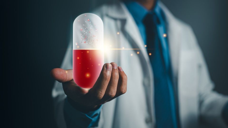 Doctor in a white coat holding an oversized red and white medicinal capsule. The capsule is glowing and contains a ball and stick model. 