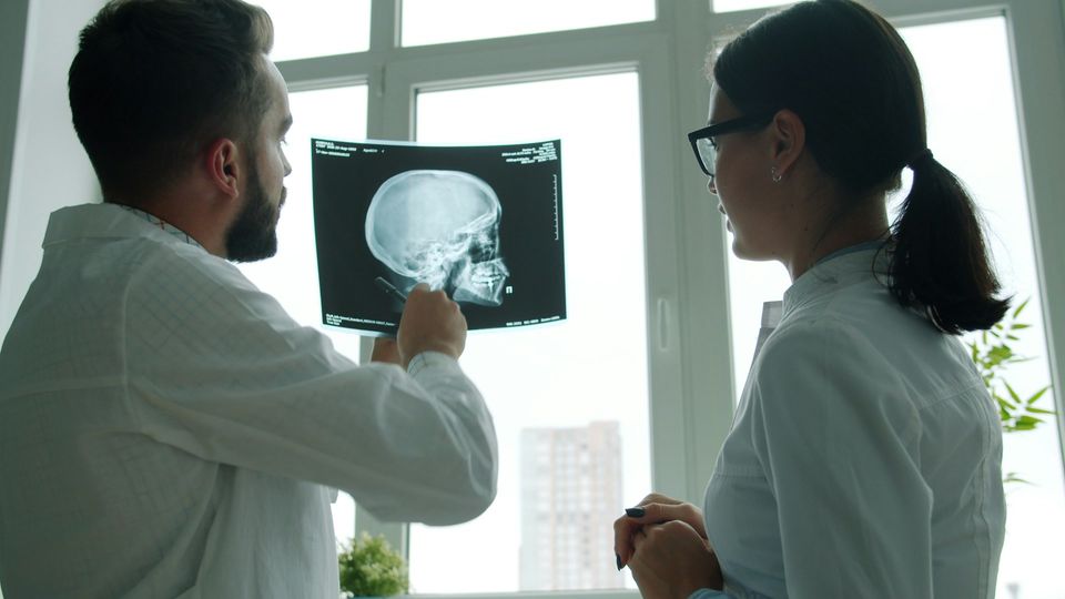 Two doctors with their back to the camera reviewing a head scan in a hospital setting.