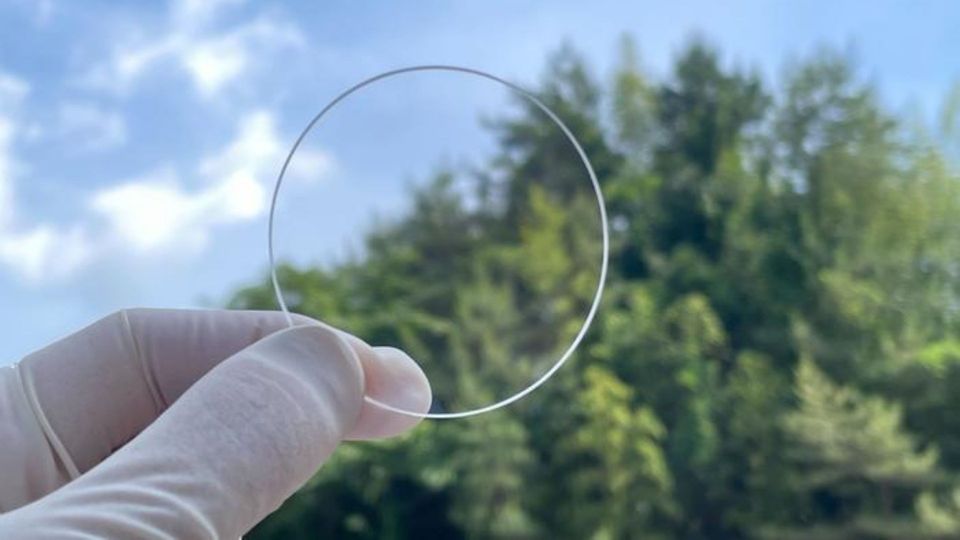 Transparent nanosheet held between gloved fingers against a forest background.