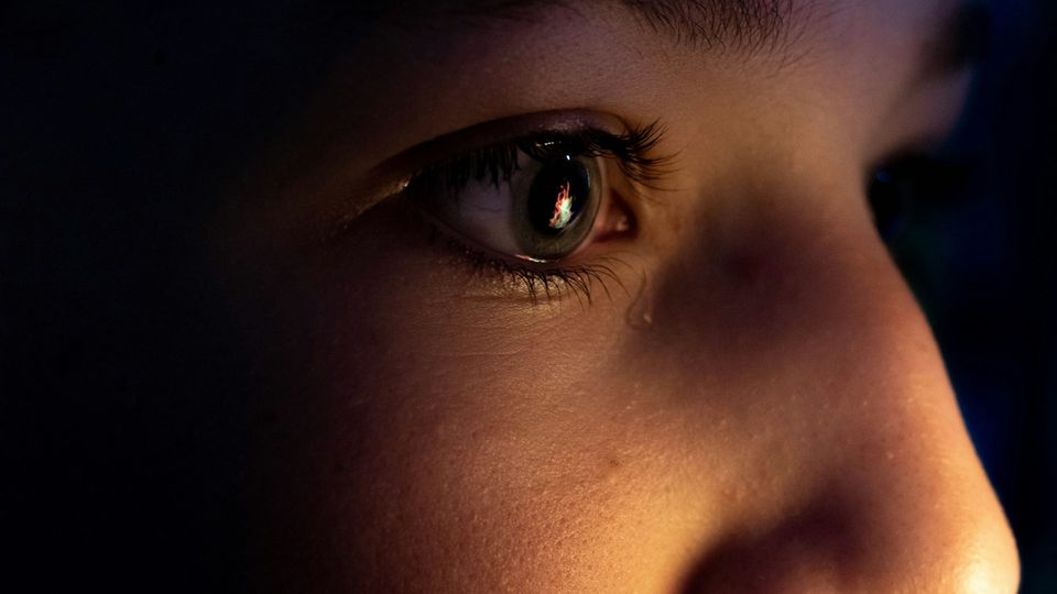 Close-up of a child's eye with a tear drop on the cheek, reflecting light in the pupil.