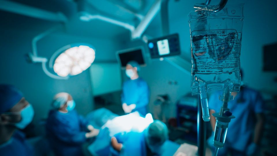 Close-up of an intravenous fluid bag with medical staff working in a hospital operating room.